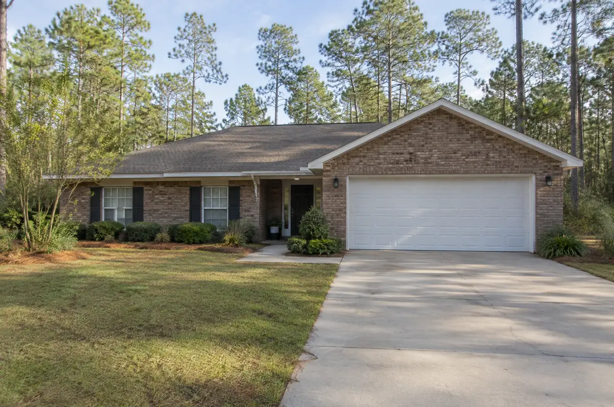 Brick ranch home with a white sectional garage door and pine trees behind it