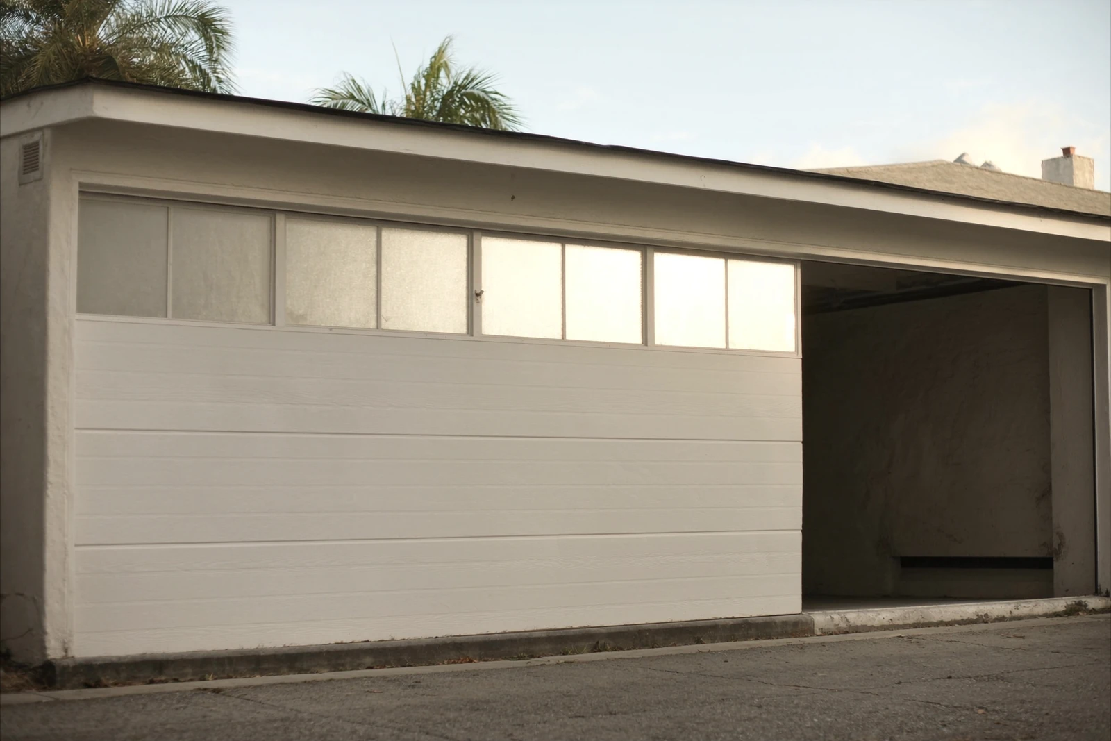 White garage door with a row of windows, partly open beside a palm tree