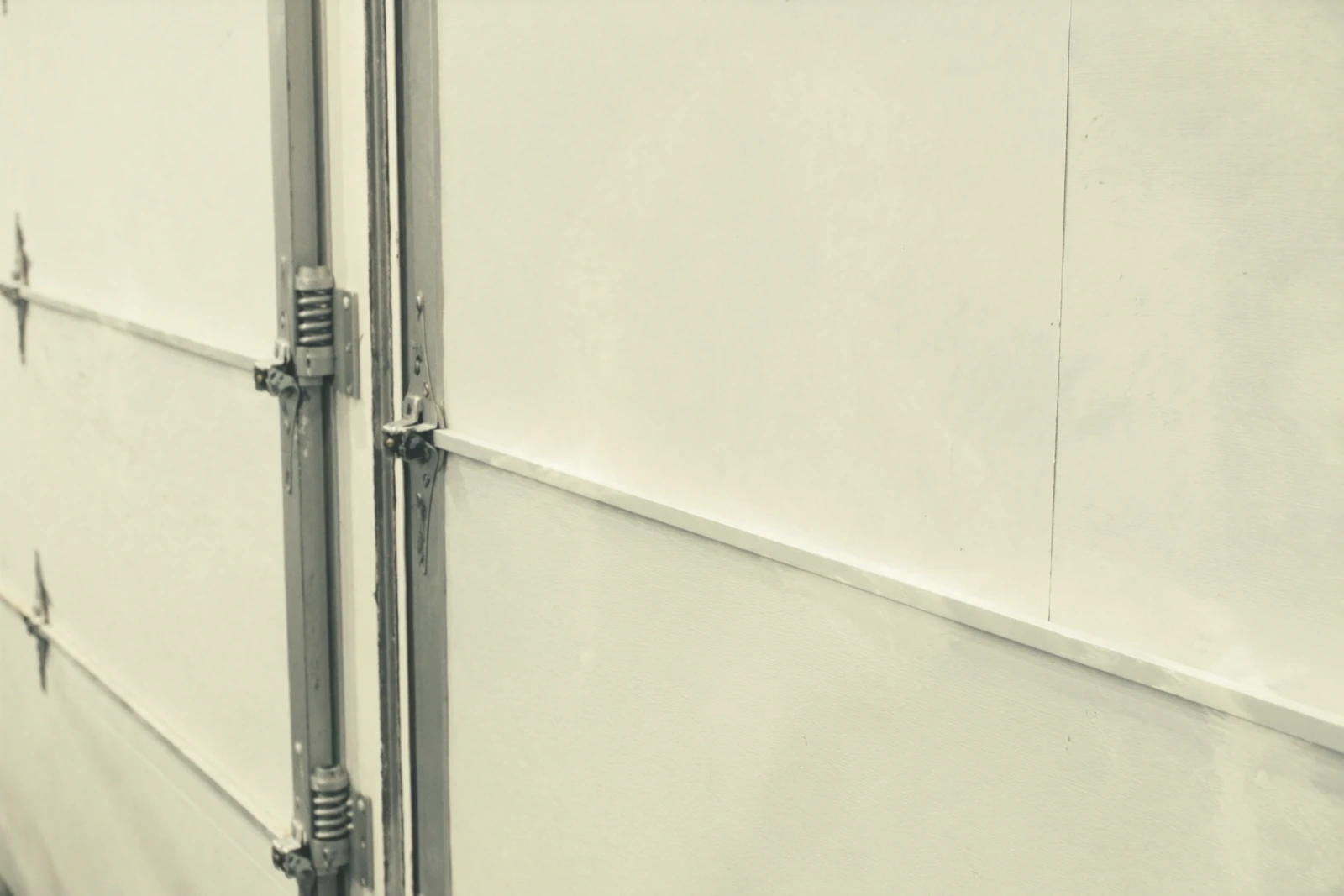 Steel hinge and roller on a white garage door section