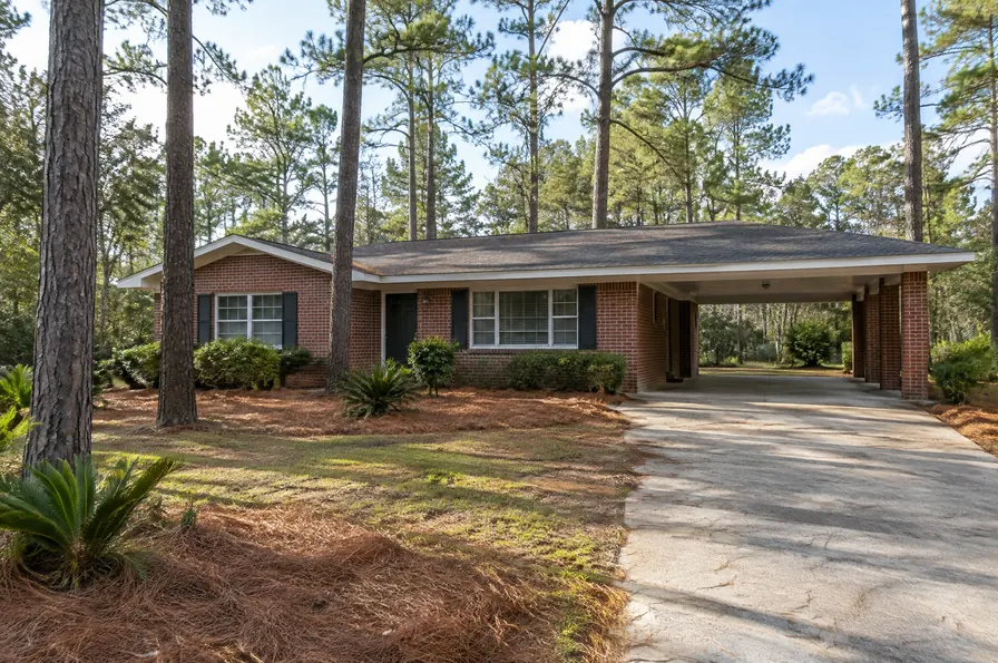 Red brick home with a carport under tall pine trees