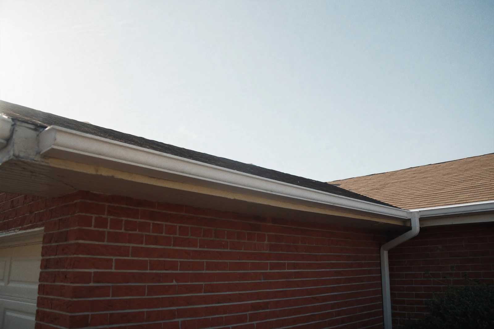 White gutter and downspout along the roofline of a red brick ranch house