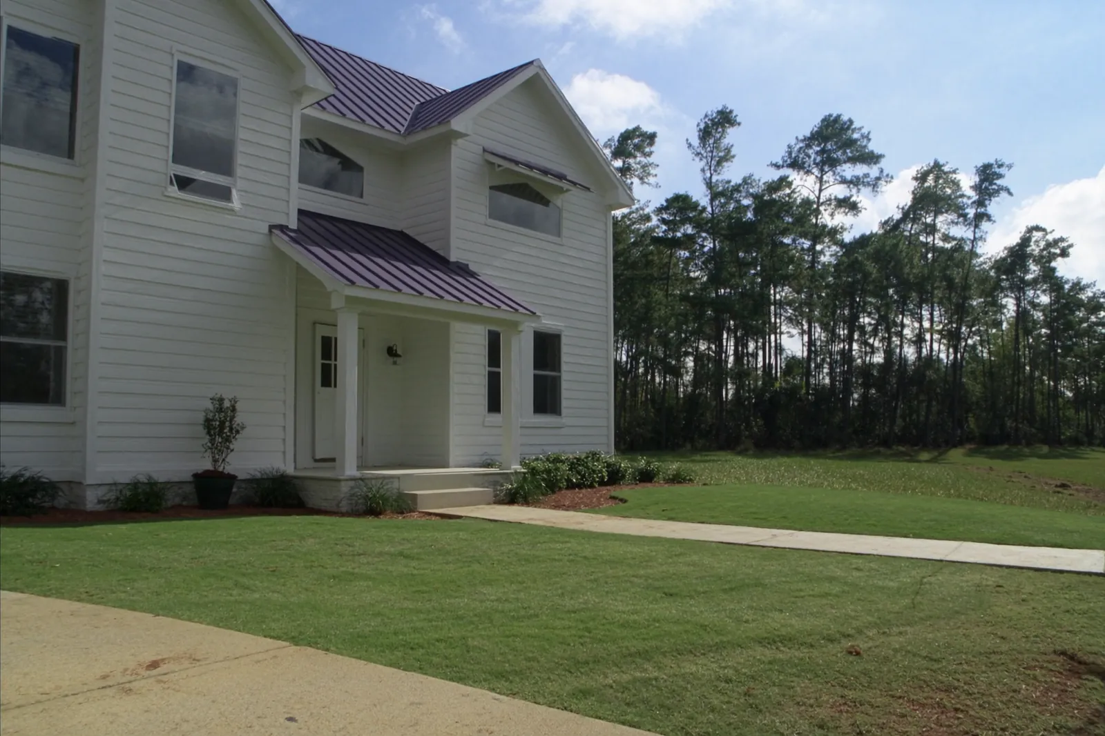 Newly built white farmhouse-style home with a metal porch roof and fresh sod