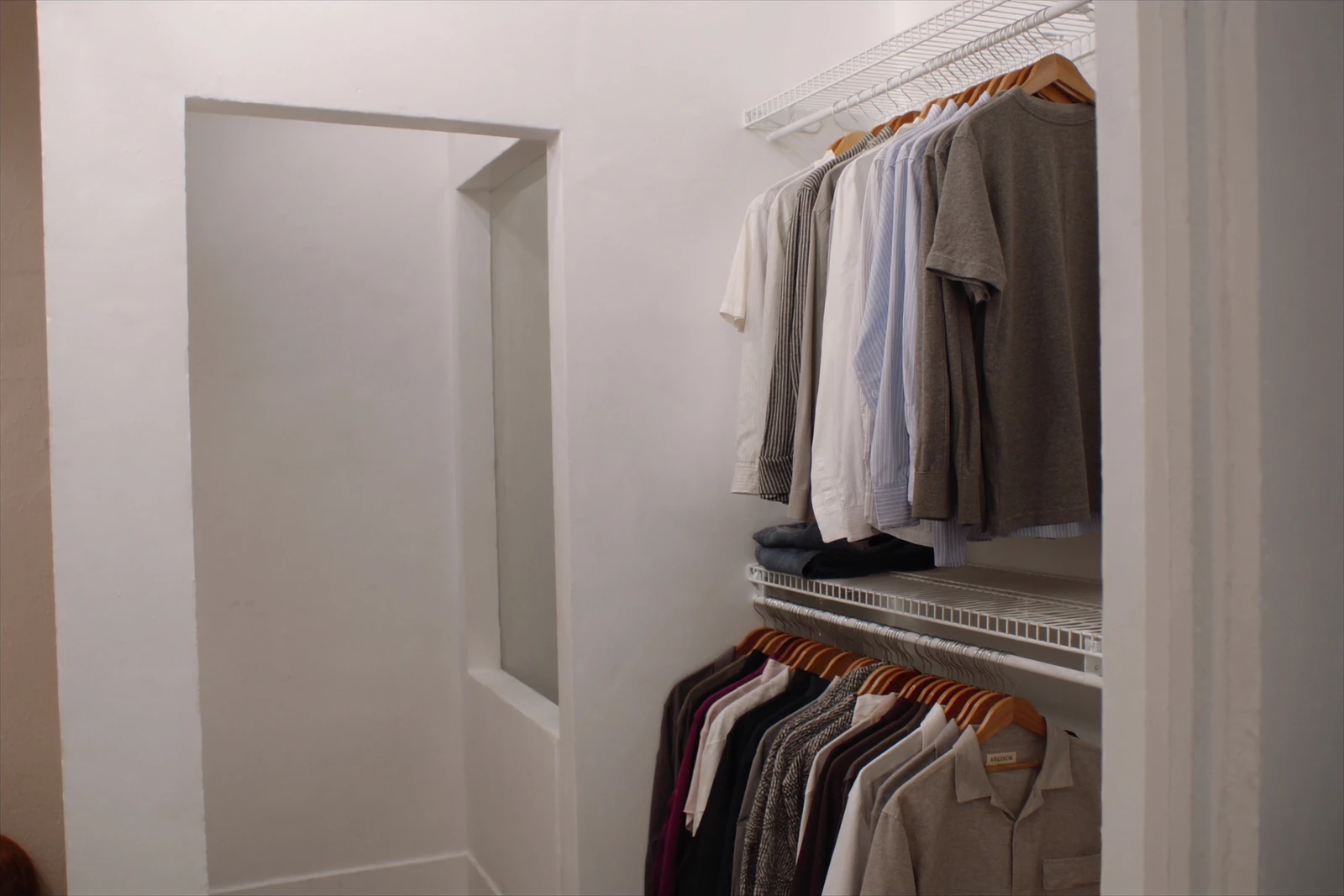Bedroom closet with white wire shelving above two rods of hanging shirts
