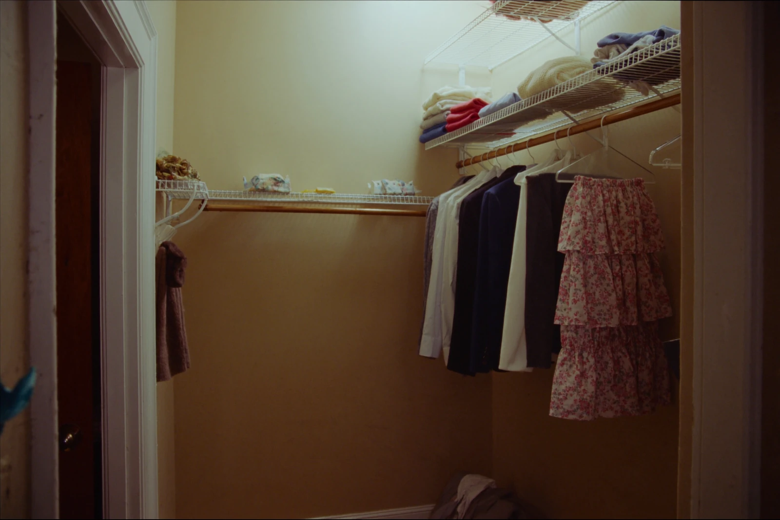 Corner closet with wire shelving holding hanging clothes and folded sweaters