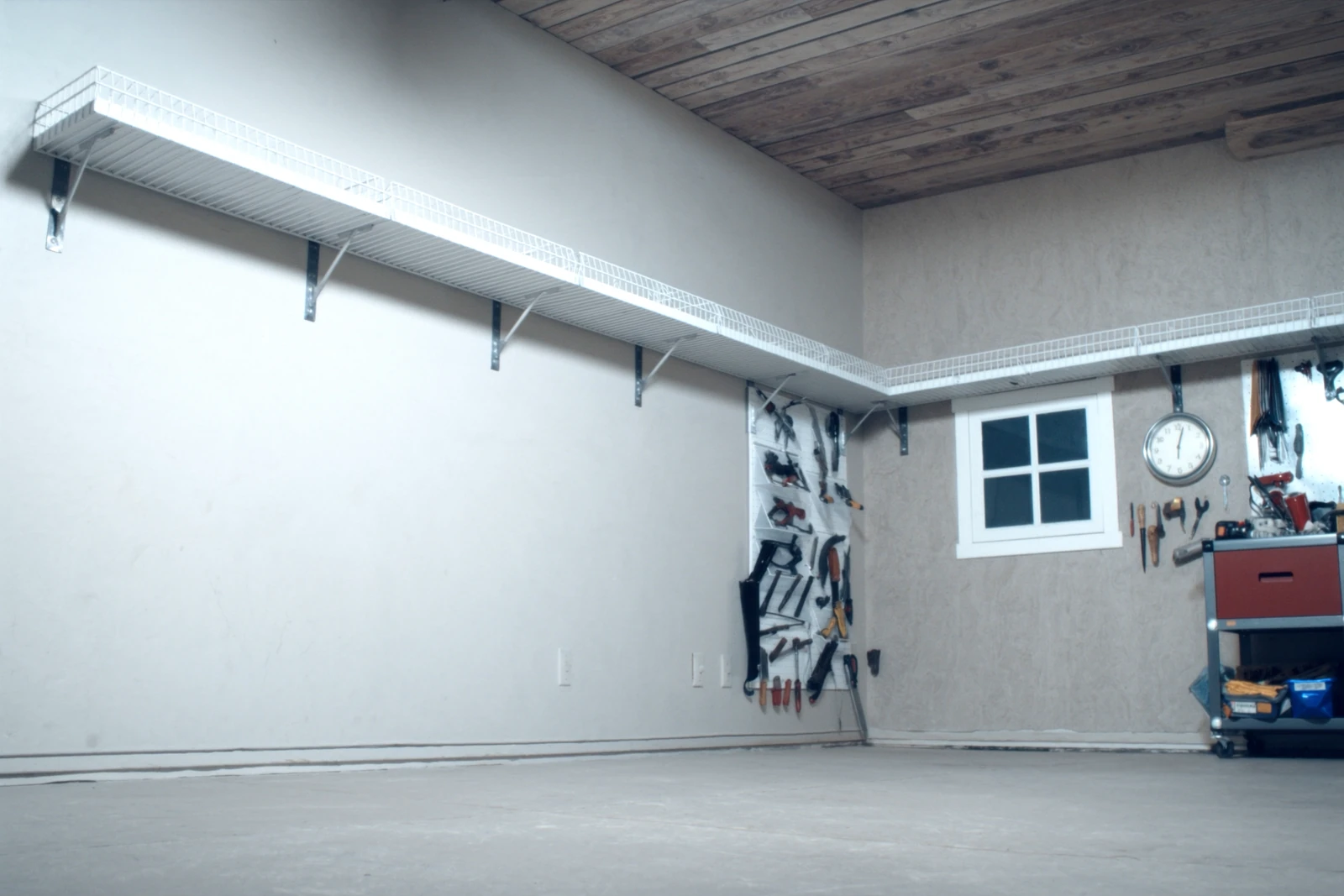 Garage wall with a long wire shelf mounted high above a workbench and hanging tools