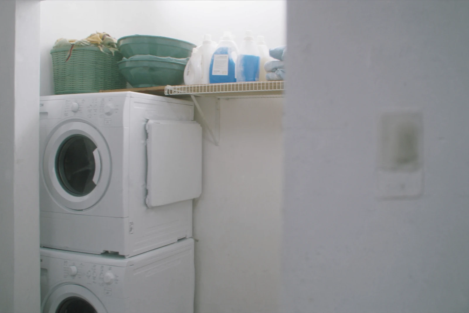 Laundry closet with a stacked washer and dryer and a wire shelf above